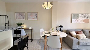Ett modernt vardagsrum med en matplats, med en bänkskiva i marmor, vita stolar, en grå soffa och konstverk på väggarna.