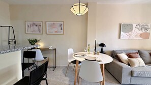 Ein modernes Wohnzimmer mit Essbereich, ausgestattet mit einer Marmorplatte, weißen Stühlen, einem grauen Sofa und Kunstwerken an den Wänden.