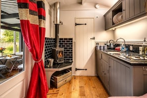 Une cuisine compacte avec un poêle à bois, un coin repas avec une table et des chaises, et une vue par la fenêtre.