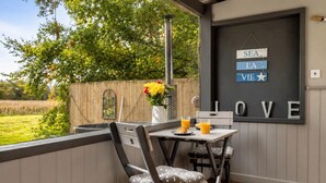 A patio with a table and chairs, a hanging sign with words, and a view of greenery.