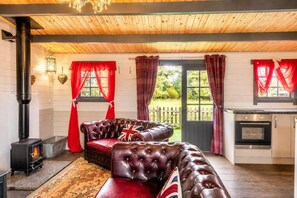 A cozy room with a fireplace, a leather sofa, a kitchen area, and a view of the outdoors. - 1 Bed in Thetford (oc-d33638) (Thompson)
