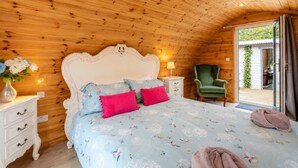 Ein Schlafzimmer mit Holzboden, einem Bett mit Blumenmuster, einem grünen Sessel und einem Nachttisch mit Lampe.