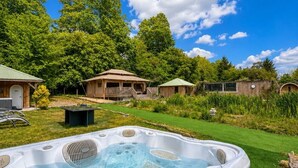Ein Whirlpool in einem Garten mit blauem Himmel, umgeben von Bäumen und einem Haus.