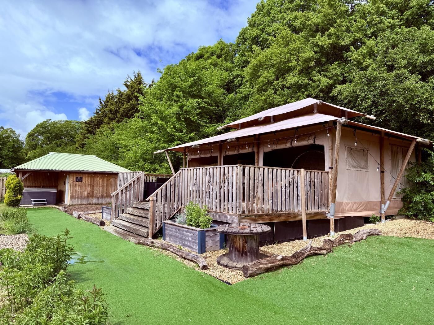 Une cabane en bois rustique avec un porche, un bâtiment séparé doté d’un toit végétalisé et une pelouse bien entretenue.