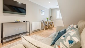 Ein modernes Wohnzimmer mit Fernseher, einem Esstisch und einer Couch.