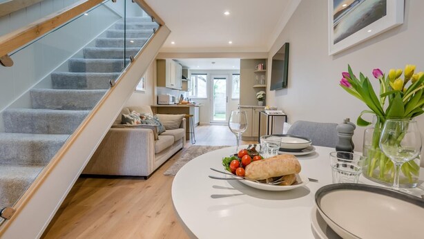 Ein modernes Wohnzimmer mit Treppe, einem Essbereich mit Tisch für zwei Personen und einer Küche im Hintergrund.