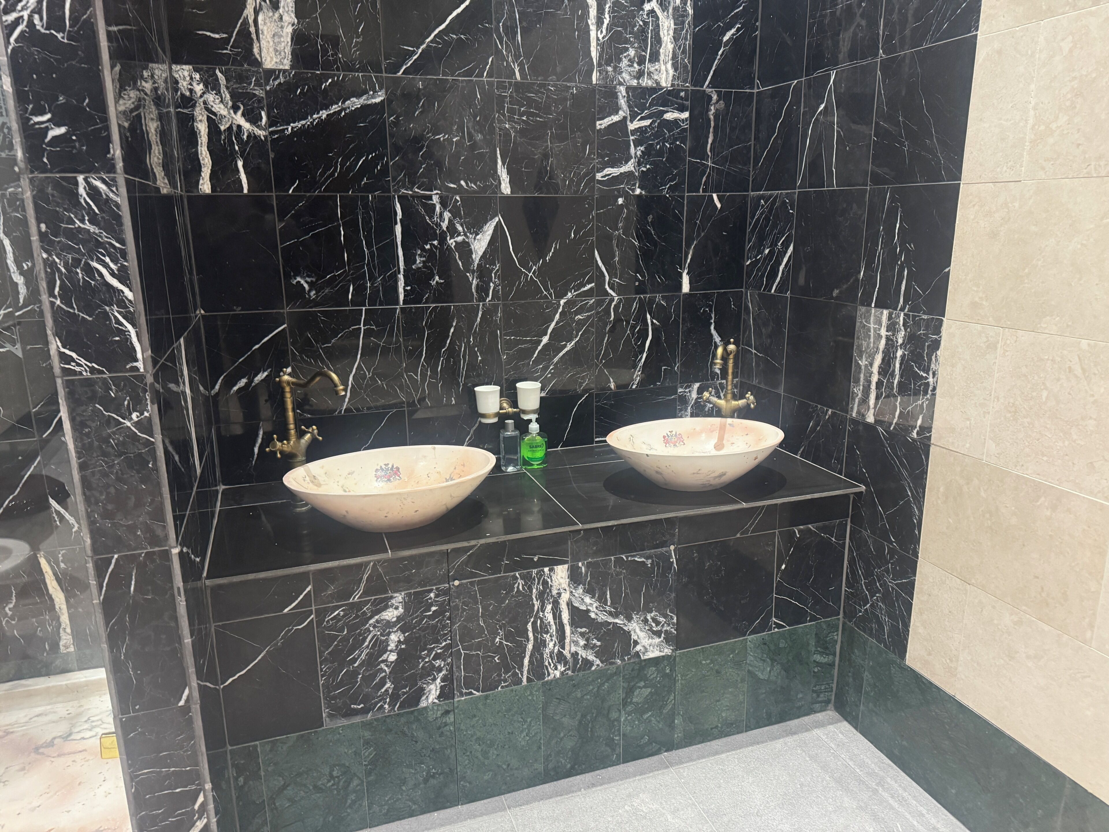 Ein Badezimmer mit zwei Waschbecken, schwarzen Marmorfliesen und einer grünen Akzentwand.