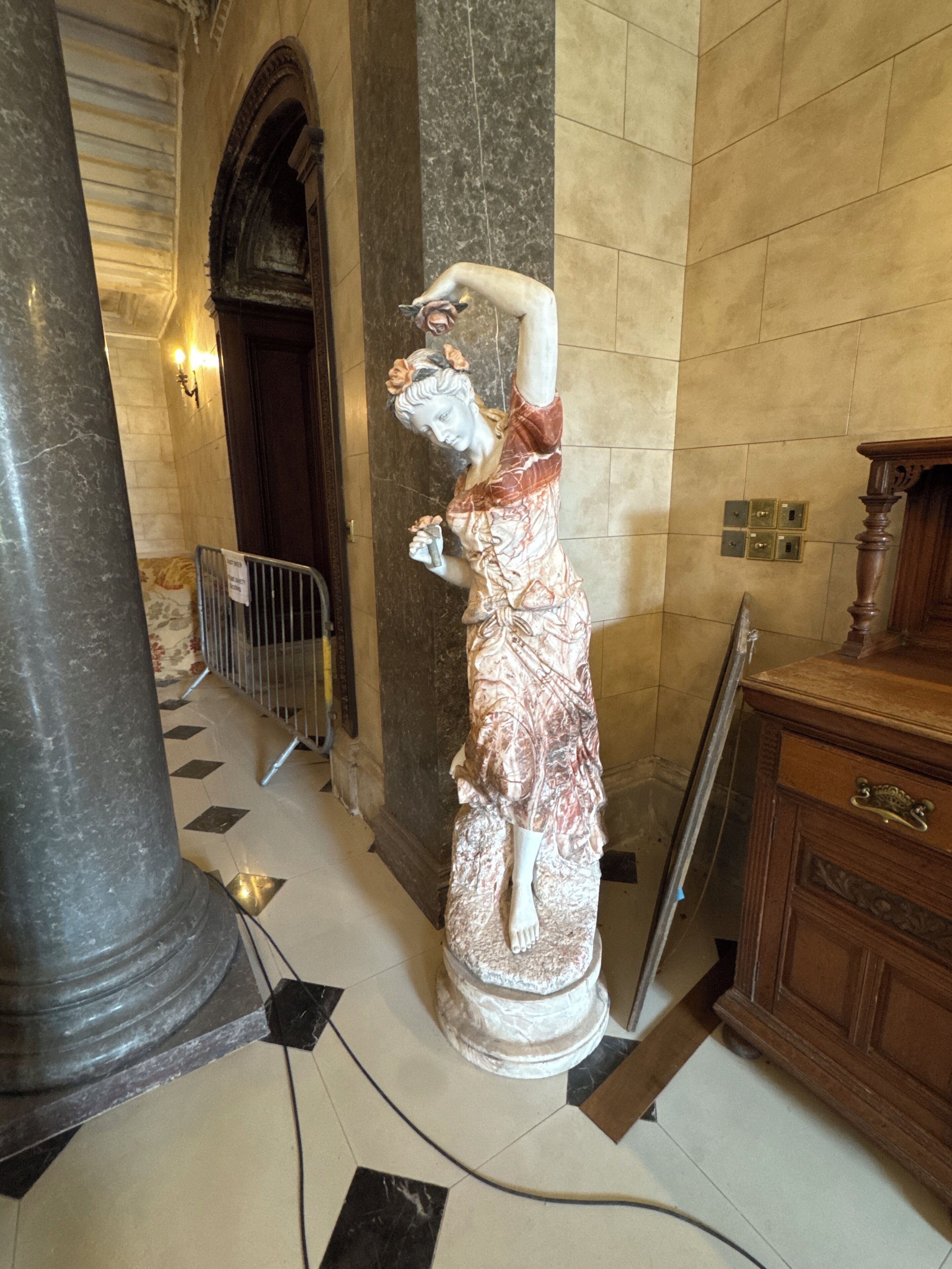 A statue in a lobby with marble columns, a wooden cabinet, and a tiled floor.