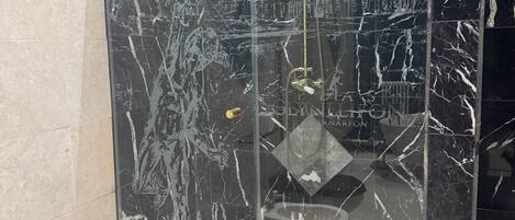 A glass-enclosed shower with a marble wall design, a gold showerhead, and a visible water control knob.