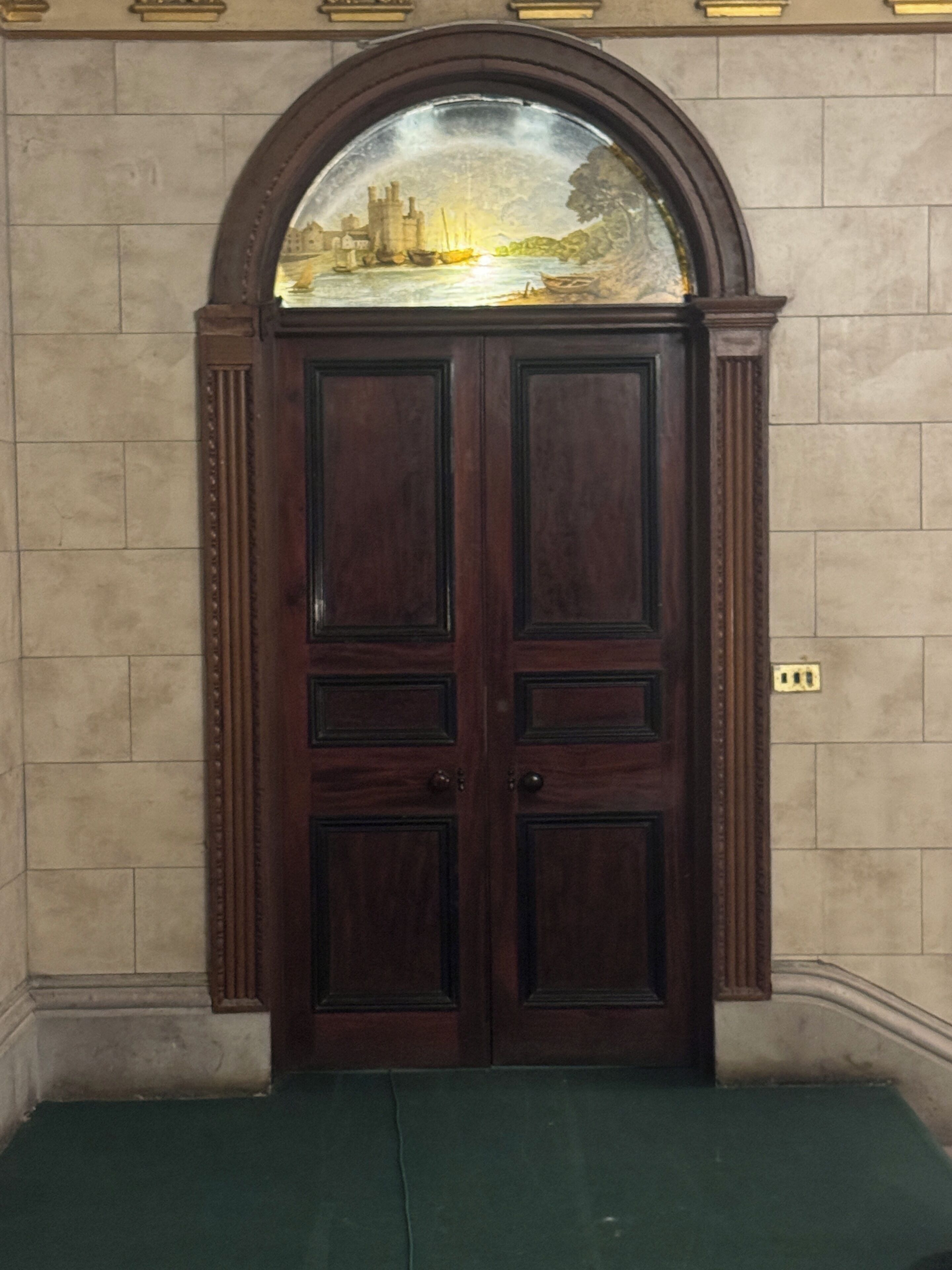 A dark wooden double door with a decorative glass window above it.