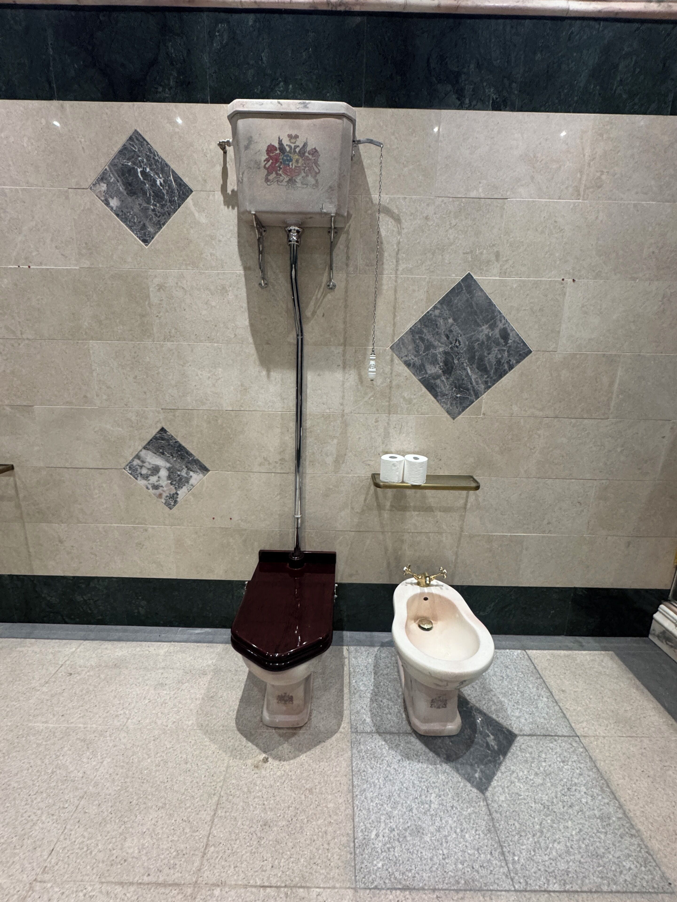 A bathroom with a toilet, bidet, and a wall-mounted bidet with a chain.