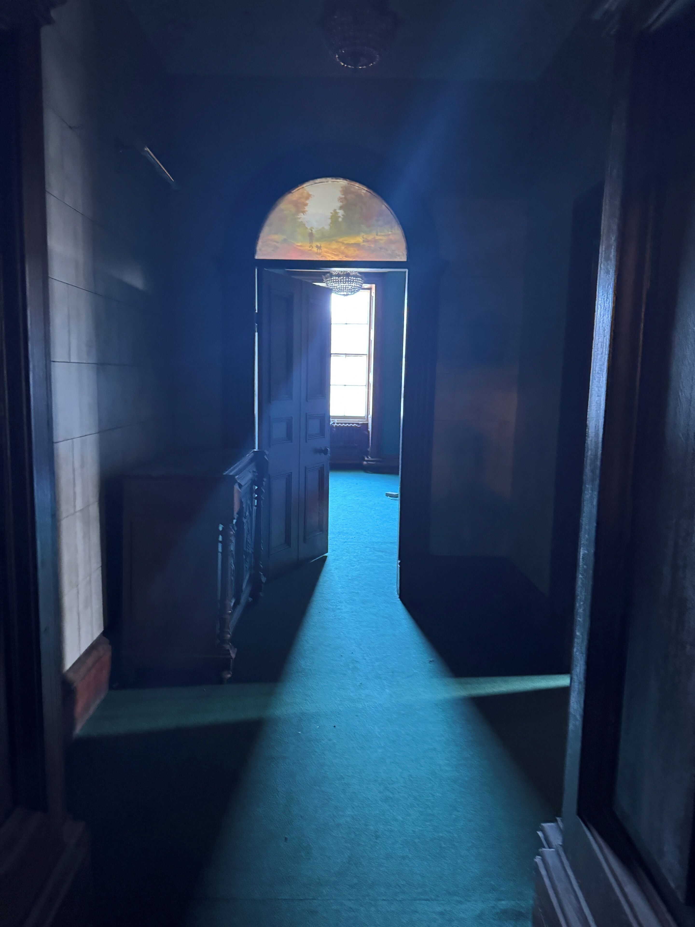 Un pasillo con alfombra azul, una puerta de madera y una ventana con vistas al cielo.