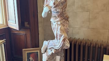 Una estatua de una mujer con vestido, de pie sobre un pedestal, con un cuadro enmarcado en el suelo a su lado.