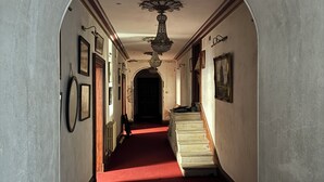Un pasillo con alfombra roja, candelabro, cuadros en las paredes y una escalera.