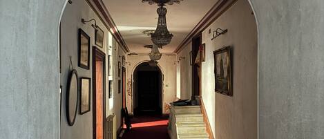 A hallway with a red carpet, a chandelier, framed pictures on the walls, and a staircase.