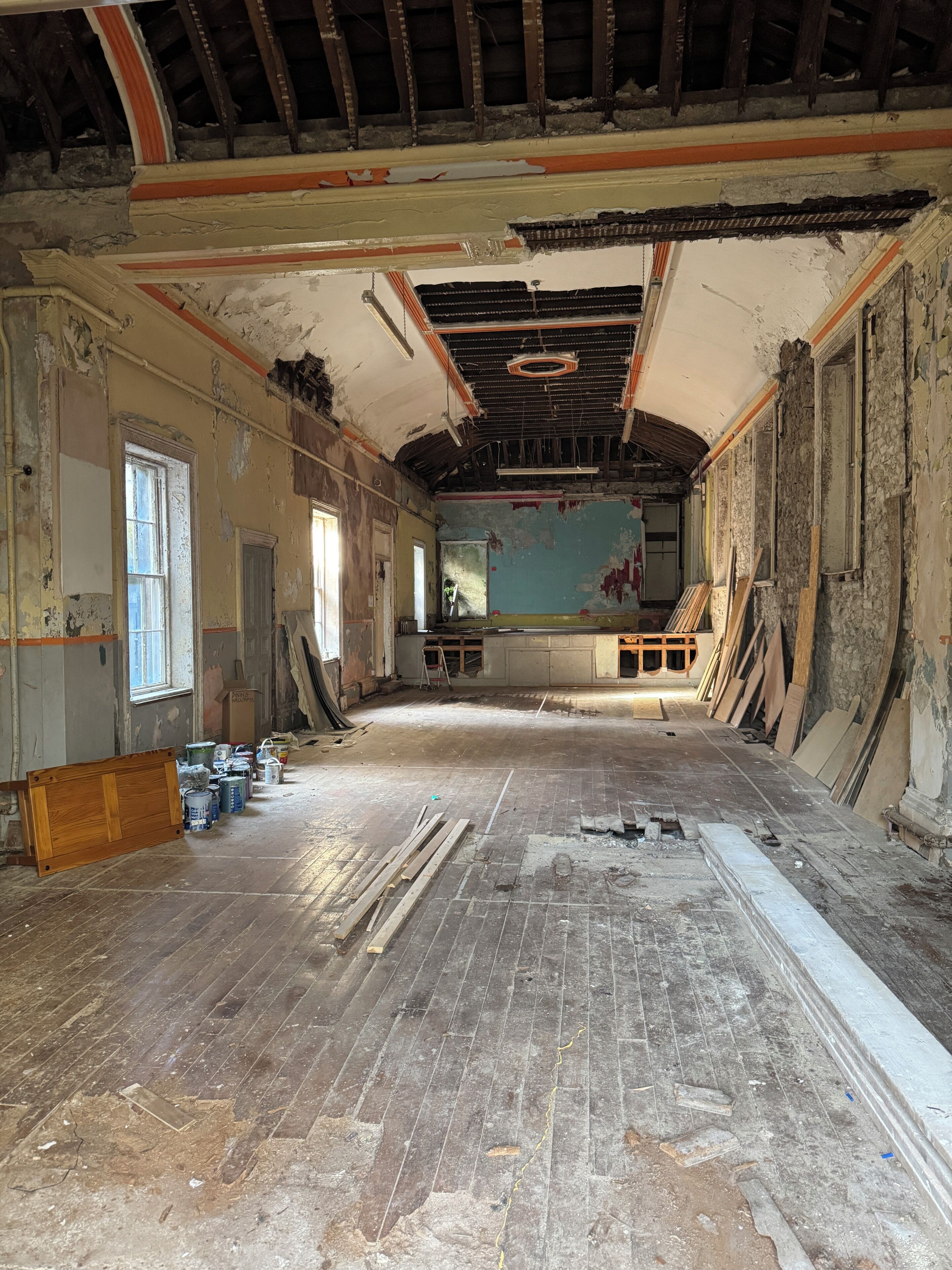 A large room with a high ceiling, exposed beams, and a partially renovated floor.