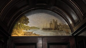 Un mural que muestra una escena junto al río con barcos y un castillo.