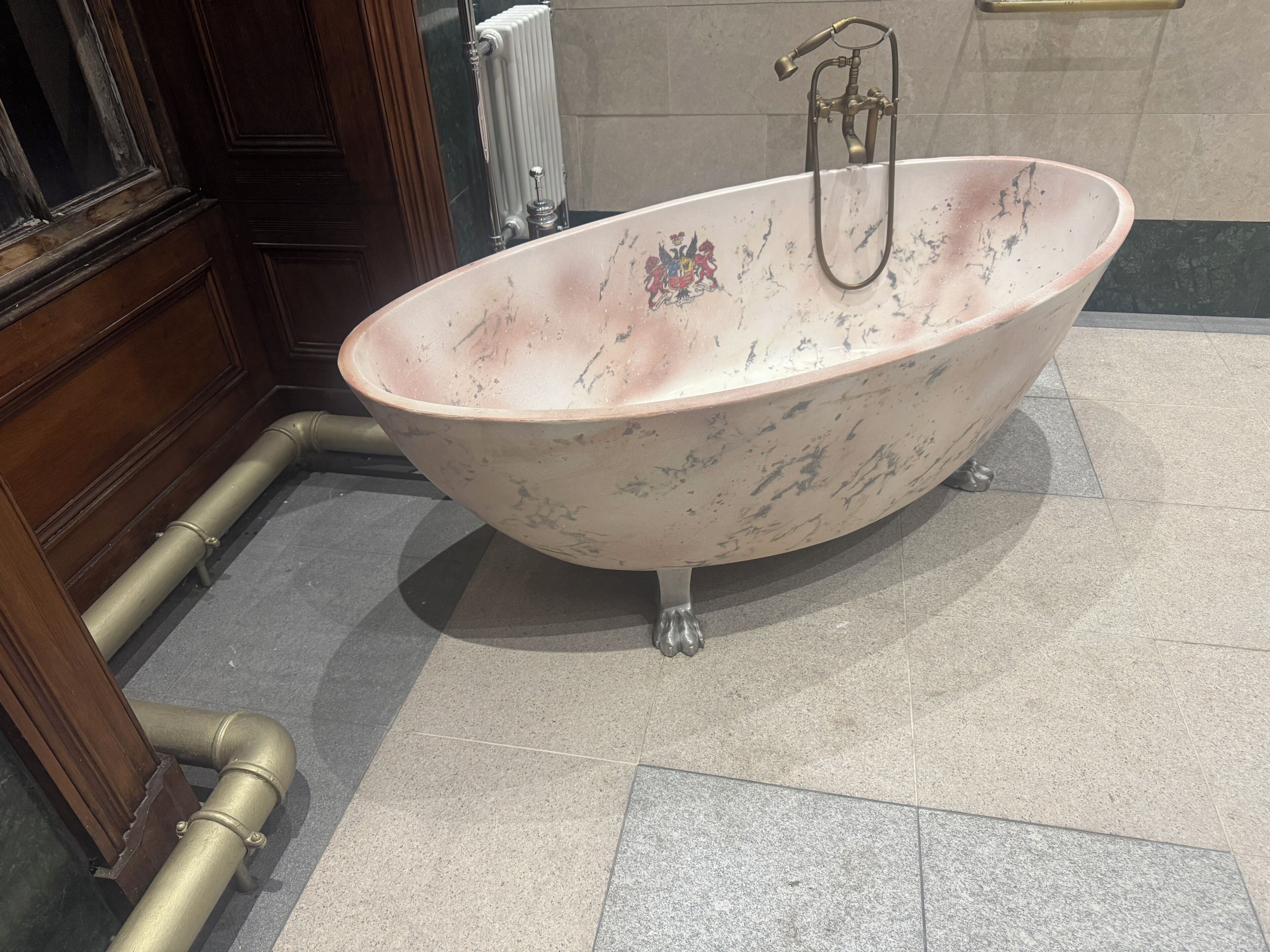 A freestanding bathtub with a shower head, positioned on a tiled floor with a radiator in the background.