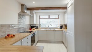 Une cuisine moderne avec des meubles blancs, un plan de travail en bois, un four encastré et une fenêtre équipée de stores.