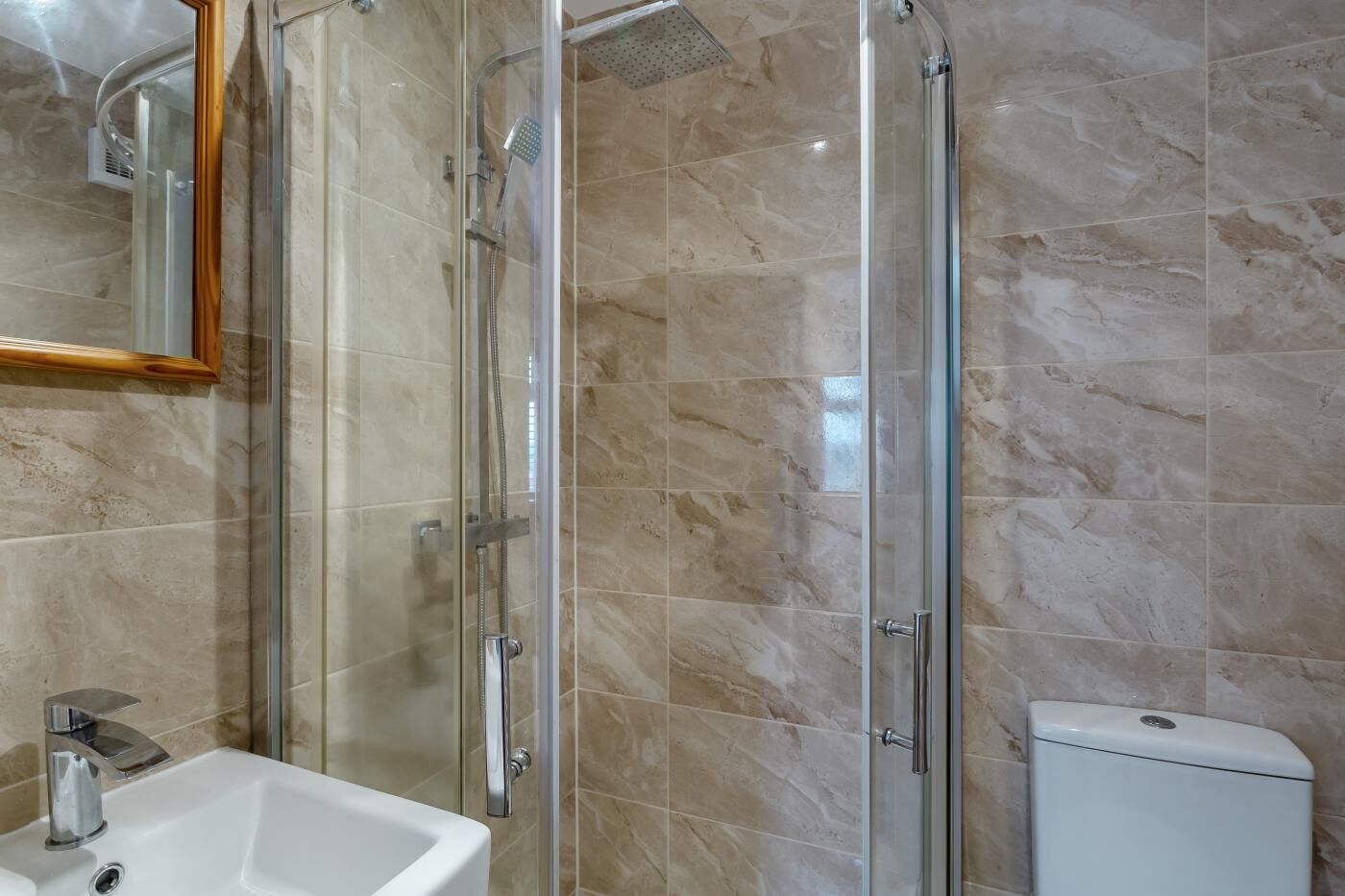 A bathroom with a glass-enclosed shower, a white sink, and a toilet.