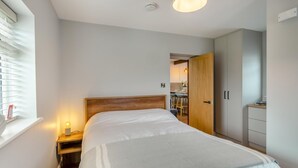 Une chambre à coucher comprenant un lit, une table de chevet, une lampe, une armoire et une fenêtre avec des stores.
