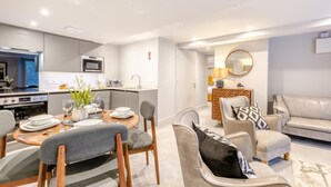 Uma sala de estar moderna com uma mesa de jantar, cadeiras, um sofá e uma área de cozinha com micro-ondas e forno.