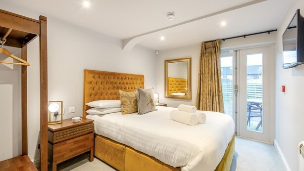 Quarto com uma cama grande, mesa de cabeceira com luminária, espelho e vista para o exterior.