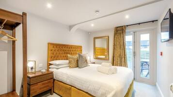 Une chambre à coucher avec un grand lit, une table de chevet avec une lampe, un miroir et une vue sur l’extérieur.