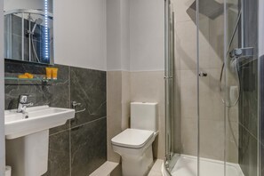 Un baño con cabina de ducha de vidrio, un lavabo blanco y un inodoro.