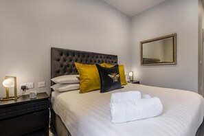 Una cama bien hecha con sábanas blancas, cabecera capitonada y almohadones decorativos en amarillo y negro.
