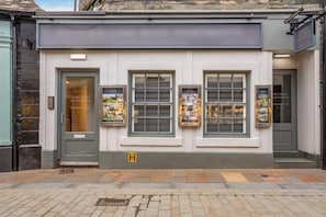A building with a grey door and windows displaying property listings. - 1 Bed in Keswick (oc-n35024) (Keswick)