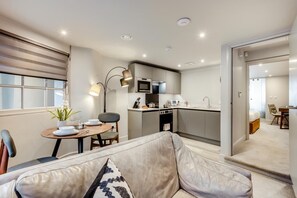 A modern apartment with a dining area, kitchen, and a living room with a sofa and a small table. - 1 Bed in Keswick (oc-n35024) (Keswick)