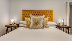 Un lit avec une tête de lit capitonnée, deux tables de chevet avec des lampes et des coussins décoratifs.