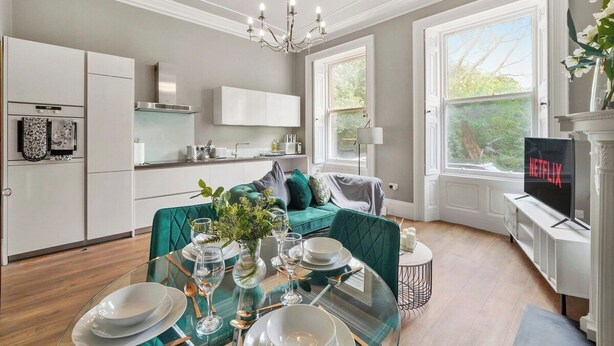 Ett modernt kök med vita skåp, en inbyggd ugn och en matplats med ett glasbord där fyra personer kan sitta.