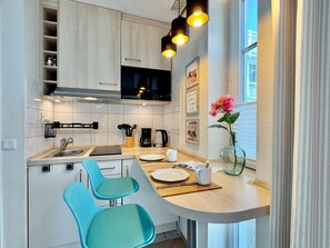 Eine moderne Küche mit Einbauherd, Mikrowelle und Kaffeemaschine. Zwei blaue Stühle und ein kleiner Esstisch mit Tellern und einer Blumenvase.