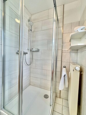 Cabina doccia con pareti in vetro, soffione a mano, porta asciugamani e termosifone.