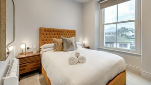 A bedroom with a large bed, a window with a view, a bedside table with a lamp, and a mirror. - 1 Bed in Keswick (oc-g35025) (Keswick)