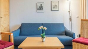 Una habitación con un sofá azul, una mesa de madera con una planta en maceta y dos cuadros en la pared.