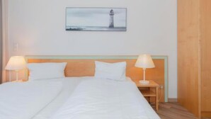 Una habitación de hotel con una cama, dos lámparas de noche, un cabecero de madera, una mesita de noche y un cuadro en la pared.