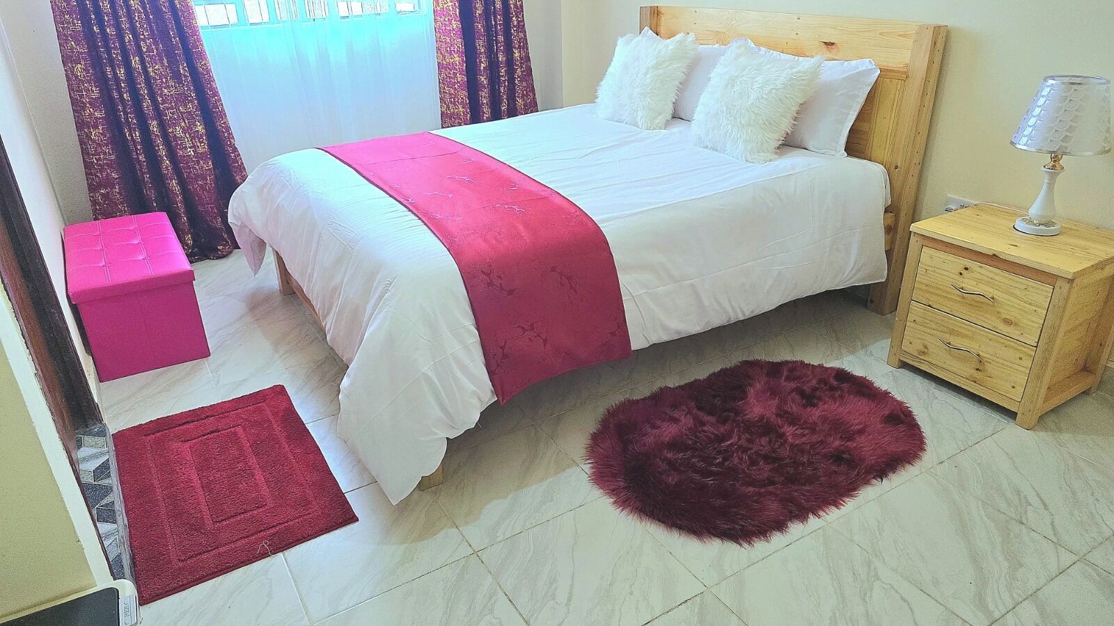 Une chambre à coucher avec un lit, une table de chevet, une tête de lit en bois, un tapis rouge et un pouf rose.