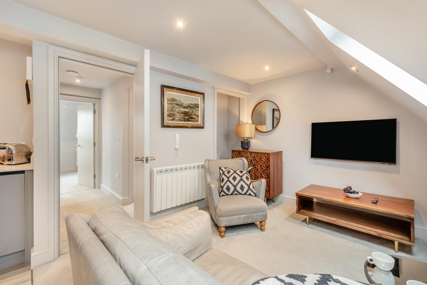 A modern living room with a sofa, armchair, and a television mounted on the wall.