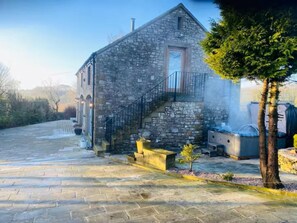 A stone building with a staircase leading to a door, a small tree, and outdoor heaters. - 3 Bed in Tideswell (oc-f35061) (Tideswell)