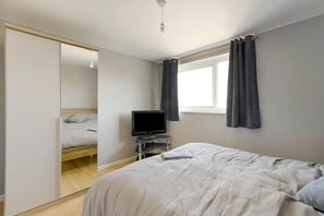 A bedroom with a bed, a television, a window with curtains, and a wardrobe. - 2 Bed in Weymouth (oc-w35035) (Weymouth)
