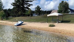 Une plage de sable avec un bateau, une tente et une zone herbeuse bordée d’arbres.