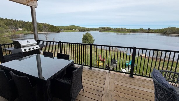 Une terrasse avec un barbecue, une table et des chaises donnant sur un lac.