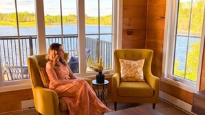 Une pièce avec vue sur un lac, un fauteuil jaune et une personne assise.