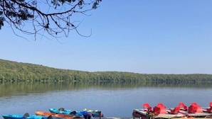 Un lac paisible où sont amarrés des kayaks et des planches à pagaie sur la rive, le tout entouré d’une forêt dense.