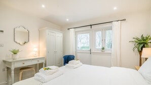 Hotellihuone, jossa on sänky, työpöytä lampun kanssa, tuoli, vaatekaappi ja ikkuna, jossa on verhot.