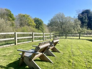 A grassy outdoor area with wooden picnic tables and a wooden fence.