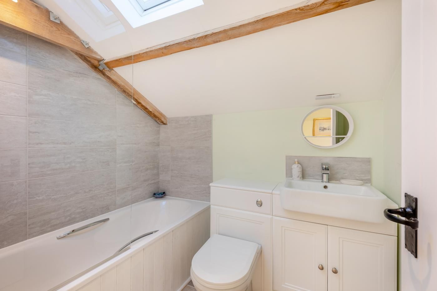 A bathroom with a skylight, a bathtub, a toilet, and a sink with a mirror.